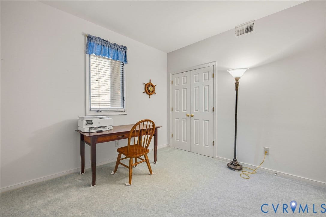 Neutral-toned interior space featuring carpeted flooring, a multi-panel door with brass-finish hardware, and a single-pane window with adjustable blinds