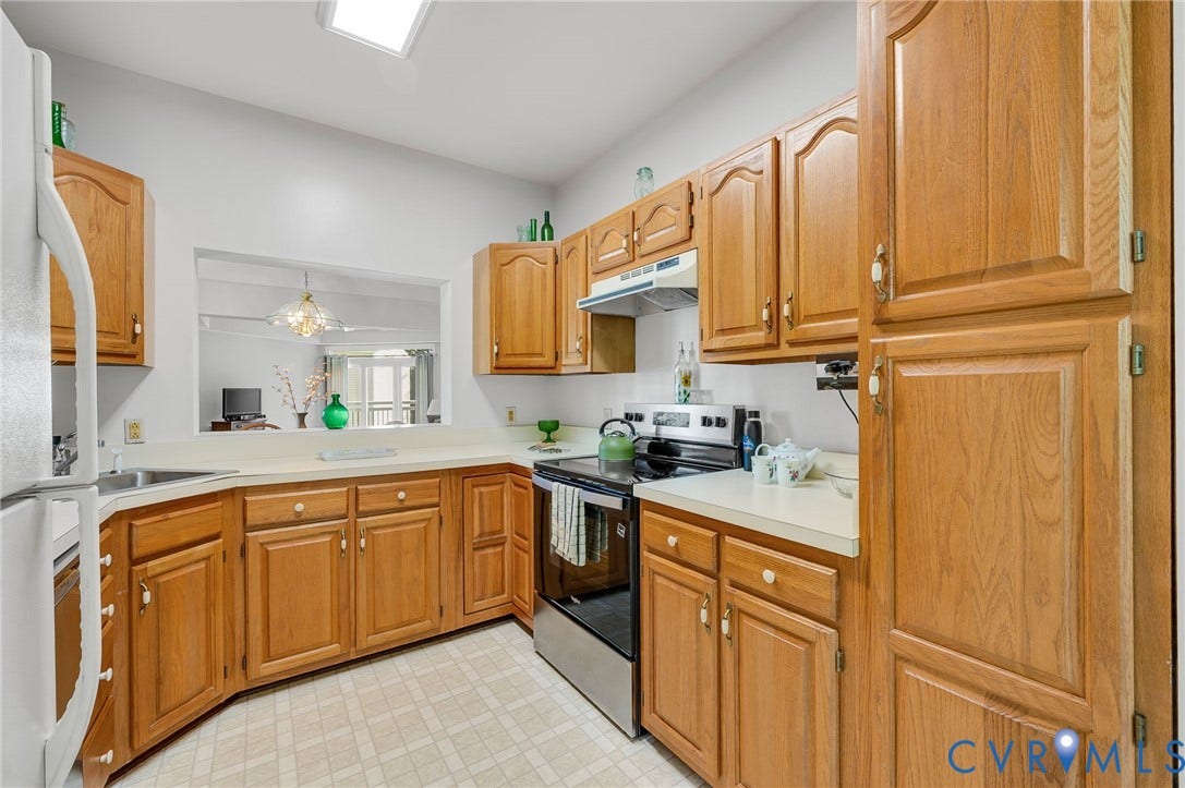 Kitchen featuring natural wood cabinetry, solid surface countertops, stainless steel appliances, and a rectangular pass-through window with a skylight above