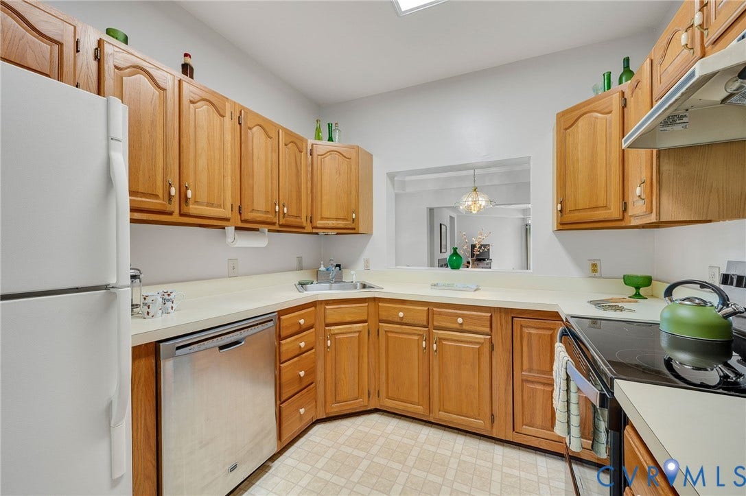 Kitchen featuring solid wood cabinetry, integrated solid-surface countertops, stainless steel dishwasher, glass-top range, and a skylight