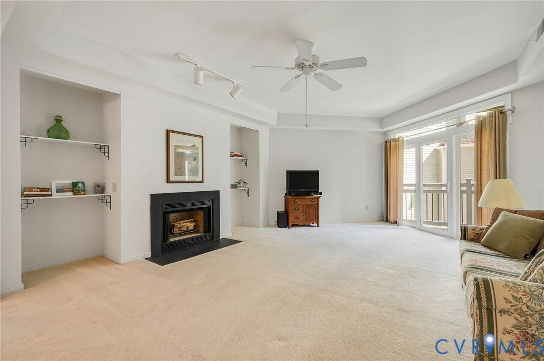 Living area featuring a fireplace with a black surround, dual recessed built-in shelving units, a ceiling fan, track lighting, and glass doors opening to a balcony
