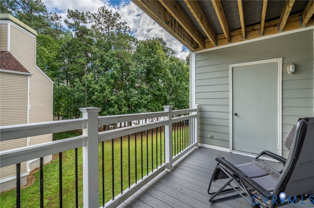 Covered balcony featuring grey composite decking, a white vinyl railing with metal balusters, and an exterior storage closet door
