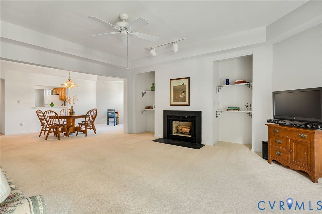 Fireplace with a black surround, recessed shelving, tray ceiling with a center fan, and track lighting