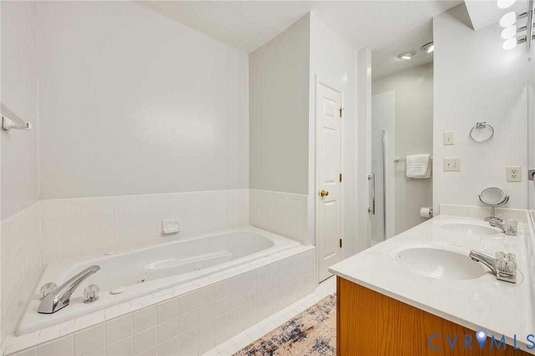 Jetted soaking tub with tile surround, dual-sink vanity with countertop, and separate glass-enclosed shower stall