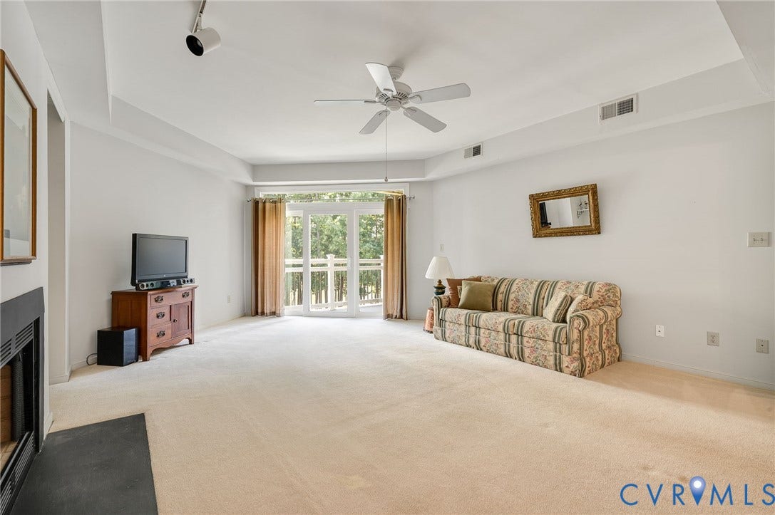 Tray ceiling featuring a central white ceiling fan, fireplace with a black surround, and glass-paneled double doors providing outdoor access