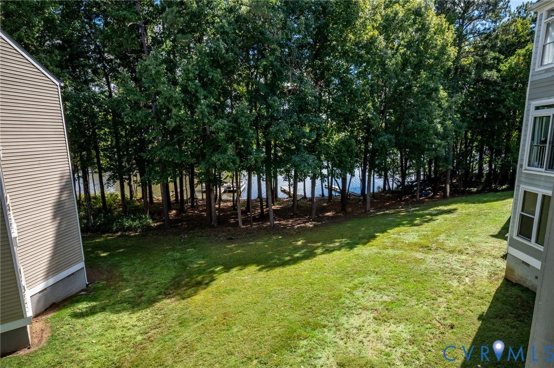 Ground-level lawn area featuring mature trees, partial water exposure, and vinyl siding exteriors