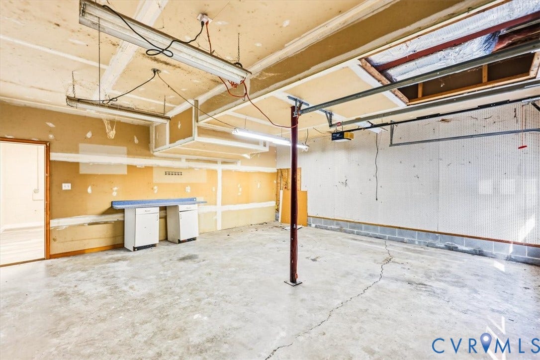 3216 Sherwood Bluff Terrace, Sherwood Bluff, Powhatan, VA 23139 Garage interior featuring concrete flooring, a central structural support column, overhead fluorescent lighting, and built-in cabinetry with a laminate countertop