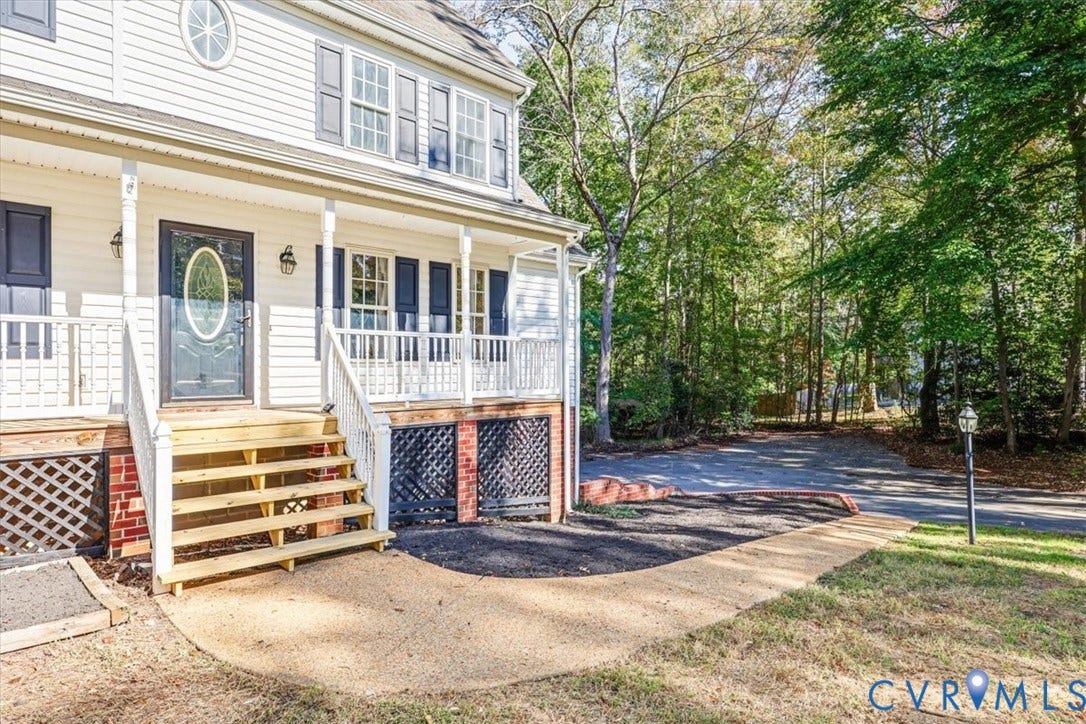 3216 Sherwood Bluff Terrace, Sherwood Bluff, Powhatan, VA 23139 Exterior facade featuring light-colored horizontal siding, a covered front porch with white railing, wood-tone steps, decorative lattice skirting, and an oval-inset entry door