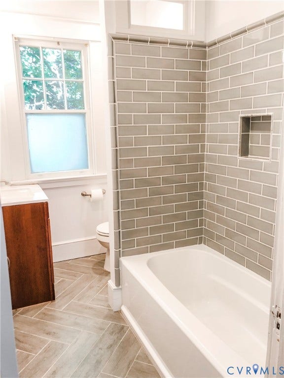 4216 Stonewall Avenue, Richmond, VA 23225 Herringbone tile flooring, subway-tiled shower with recessed niche, built-in bathtub, wood-finish vanity, and window with privacy film