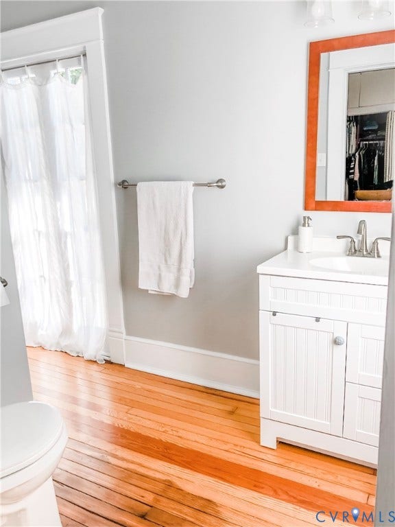 4216 Stonewall Avenue, Richmond, VA 23225 Hardwood flooring, white vanity with beadboard detailing, white countertop, chrome faucet, and a wall-mounted mirror with an orange frame