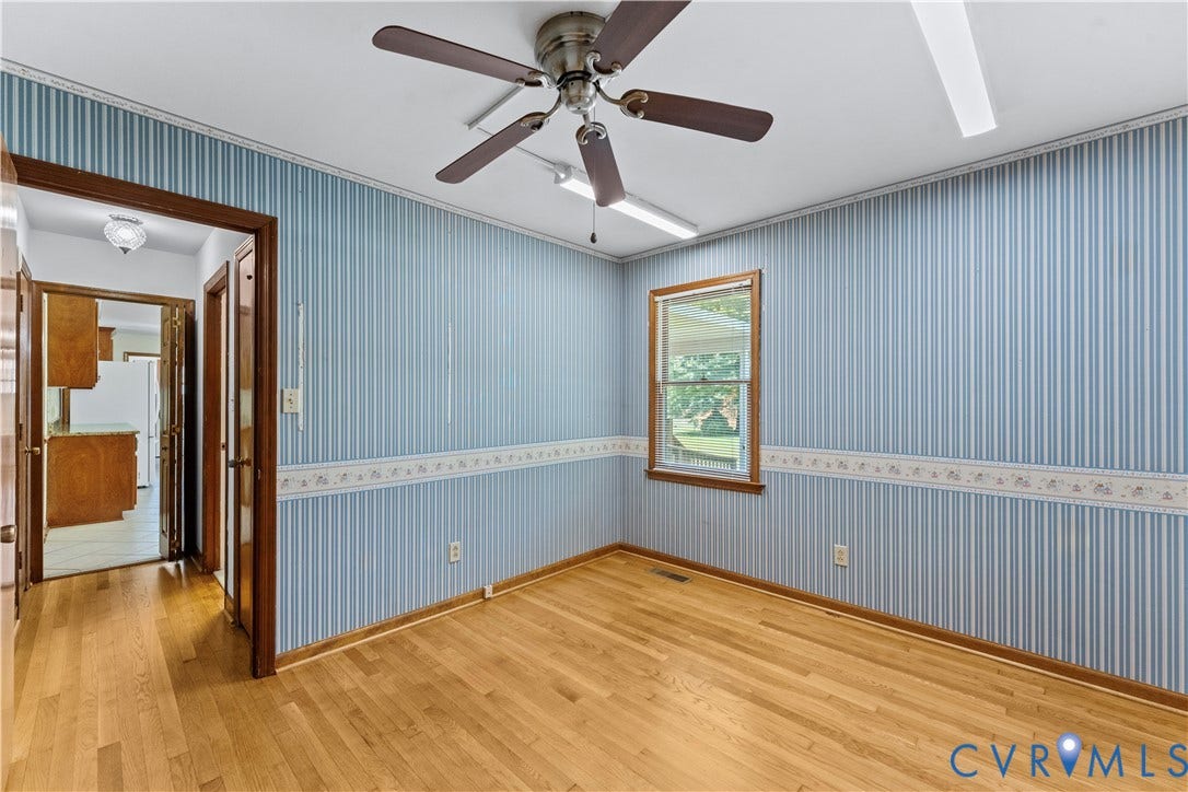 11612 Yorkdale Drive, Rivers Edge, North Prince George, VA 23860 Bright bedroom featuring light blue vertical striped wallpaper with coordinating chair rail detail, wood-finish flooring, ceiling fan with integrated lighting, and a wood-framed window with natural light