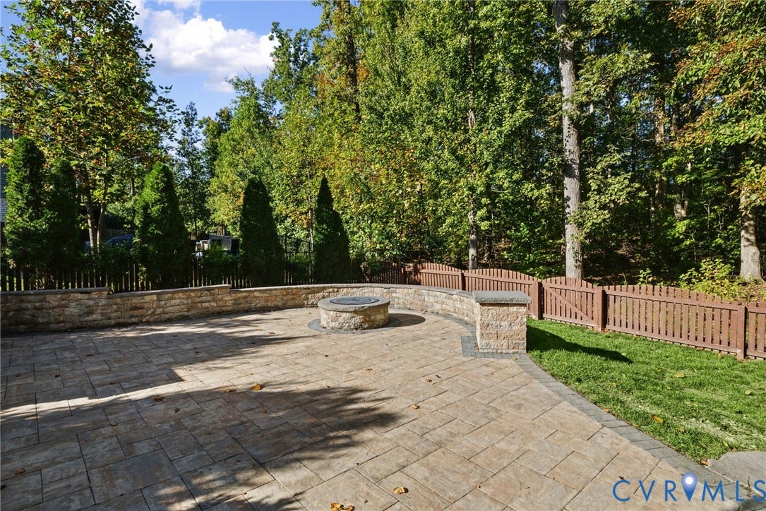 1425 Montcroft Way, Midlothian, VA 23112 Paver patio featuring a built-in stone fire pit, tiered stone retaining wall, and wooden perimeter fencing