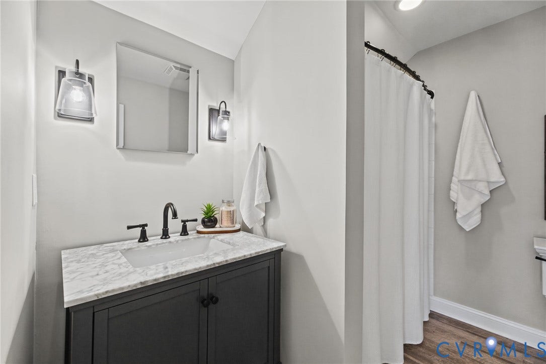 1425 Montcroft Way, Midlothian, VA 23112 Bathroom vanity featuring a dark-finish cabinet, stone-patterned countertop, integrated basin, and matte black widespread faucet fixtures complemented by dual wall-mounted sconces