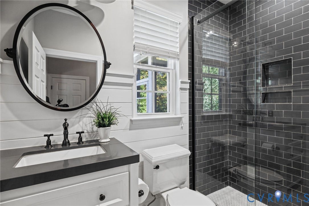 1425 Montcroft Way, Midlothian, VA 23112 Bathroom featuring white shiplap walls, a vanity with a dark countertop and a circular mirror, a glass-enclosed shower with charcoal subway tile and built-in recessed shelving, and a horizontal-slat window