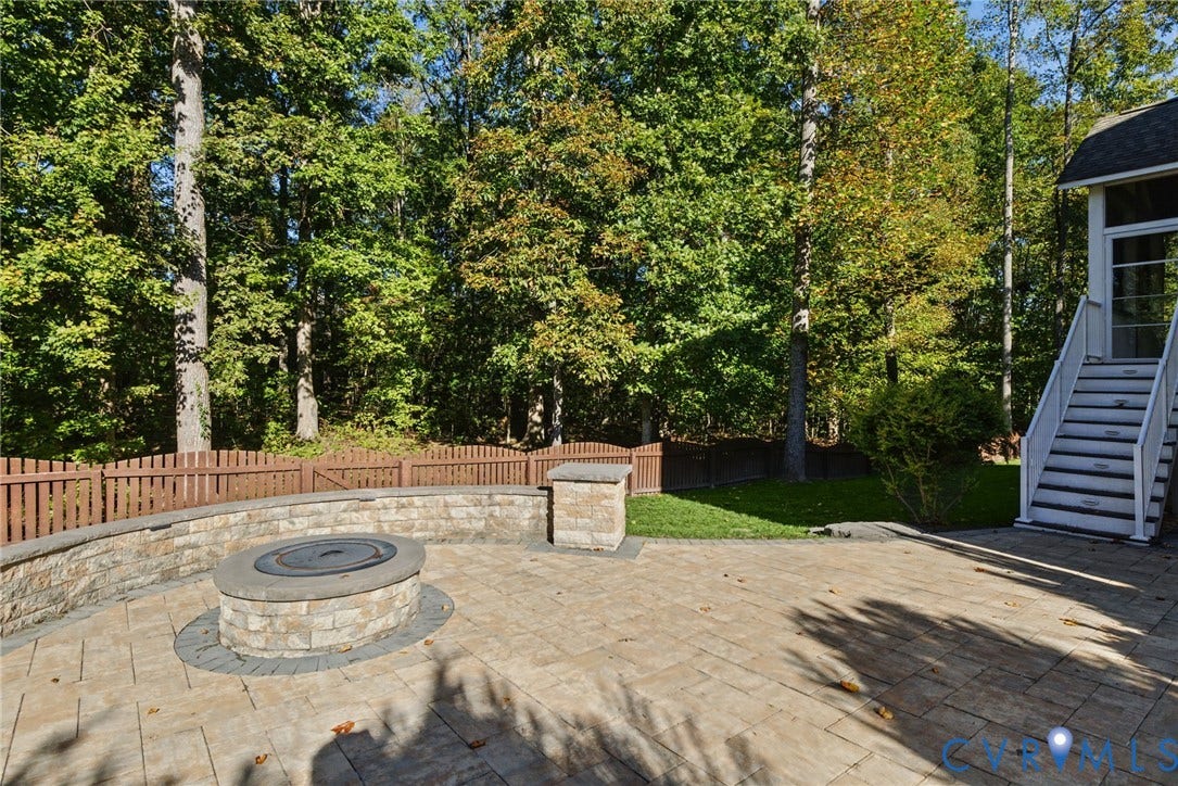 1425 Montcroft Way, Midlothian, VA 23112 Stone-paver patio featuring a circular masonry fire pit, curved stone-veneer retaining wall, wood-style privacy fencing, and exterior staircase