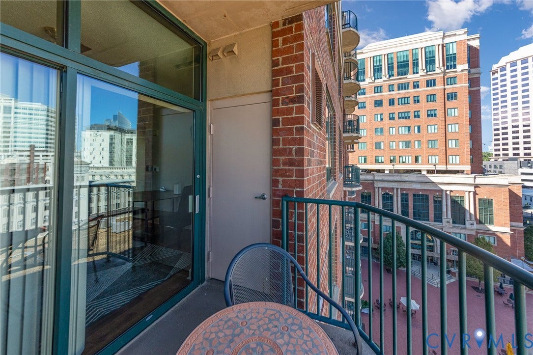 1101 Haxall Point, #709, Richmond, VA 23219 Balcony with metal railing, brick exterior, sliding glass door, and cityscape backdrop