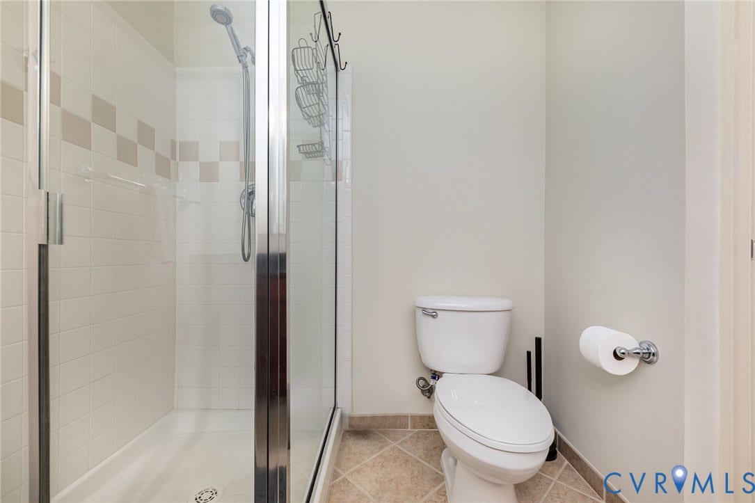 1101 Haxall Point, #709, Richmond, VA 23219 Glass-enclosed shower with a handheld showerhead, white tile surround with decorative accent tiles, and a white shower pan