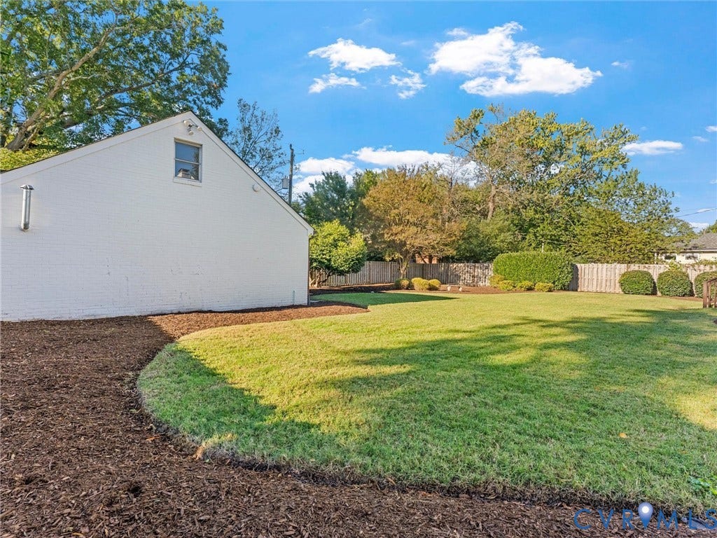 Expansive backyard featuring a manicured lawn, established landscaping, perimeter fencing, and a white-painted brick exterior