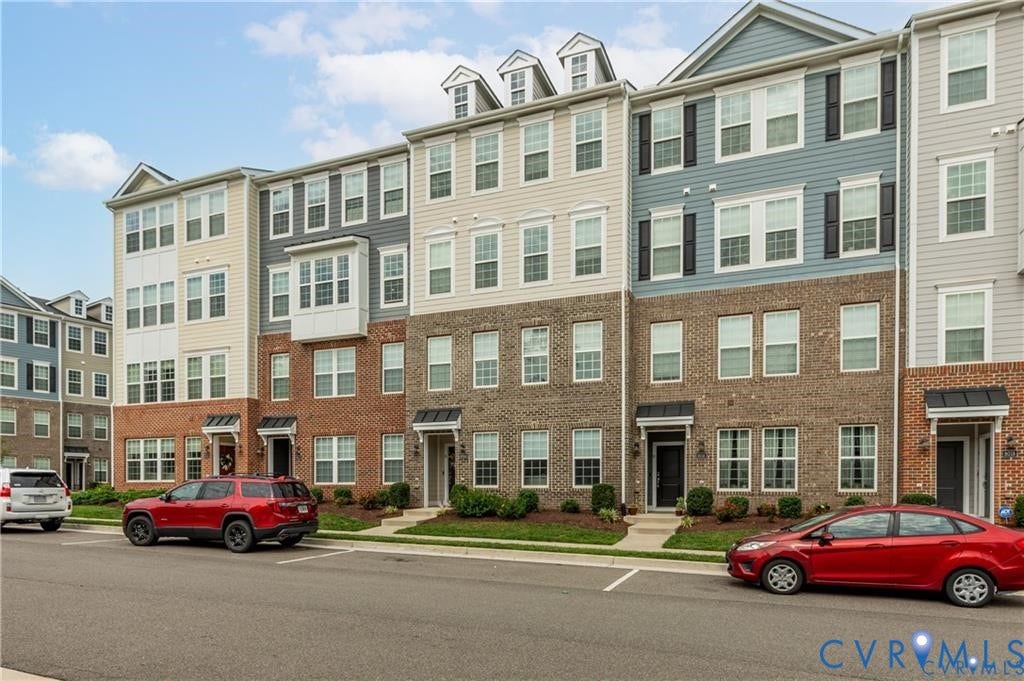 Multi-level townhome exterior featuring a combination of brick veneer and horizontal siding, prominent bay window detailing, dormer roof accents, and covered entryways