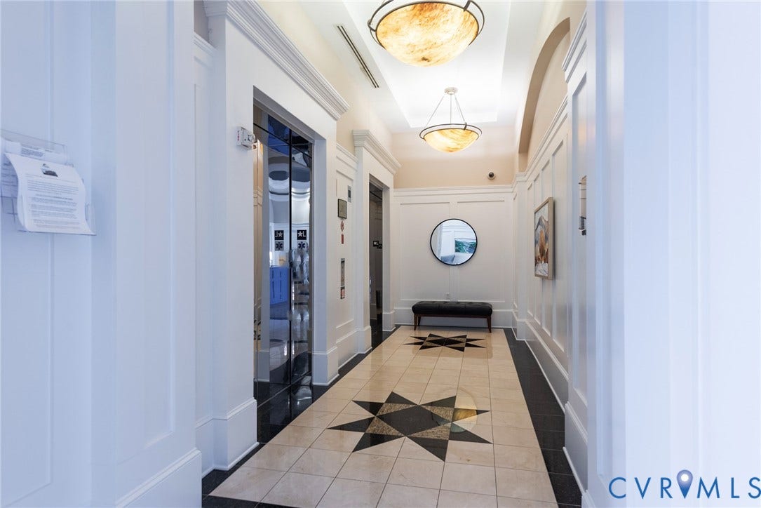 1101 Haxall Point, #511, Richmond, VA 23219 Hallway featuring two elevators with reflective doors, decorative ceiling light fixtures, wainscoting paneling, and patterned tile flooring