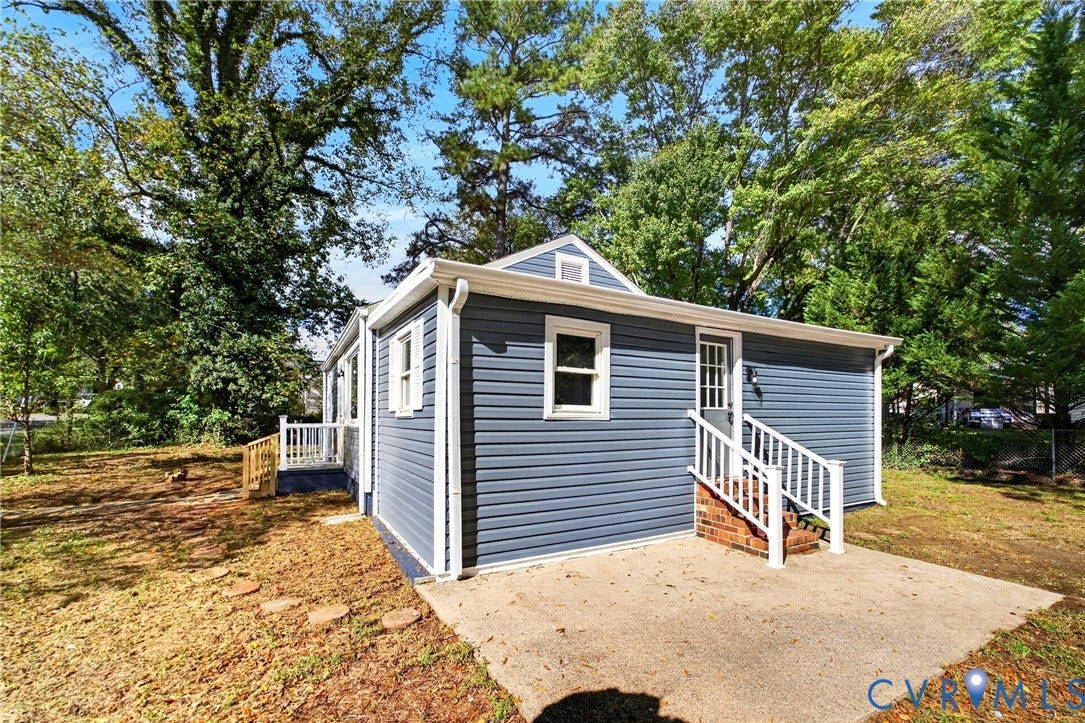 Blue horizontal siding, white trim, white gutters, concrete patio, and a white railing on brick steps