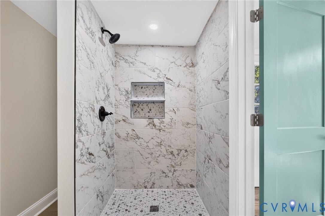 Walk-in shower with marble-look wall tiling, mosaic tile flooring, built-in recessed shelves, and matte black fixtures