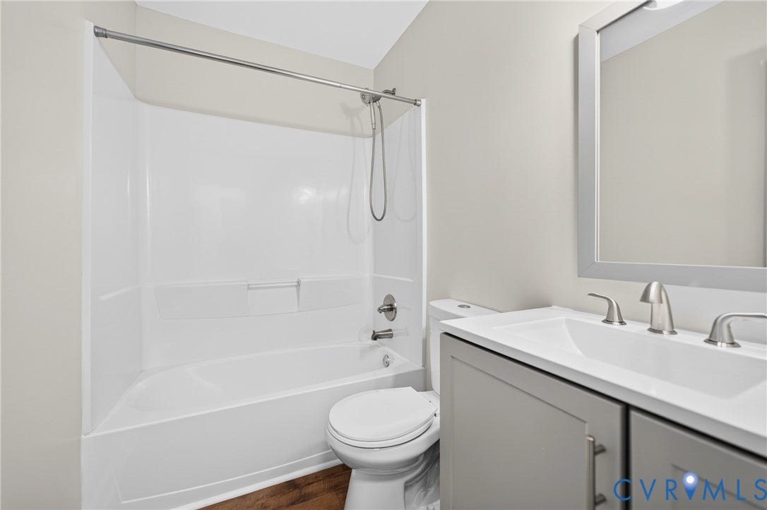 Full bathtub with an integrated shower, gray vanity with double doors, under-mount sink, and a framed mirror