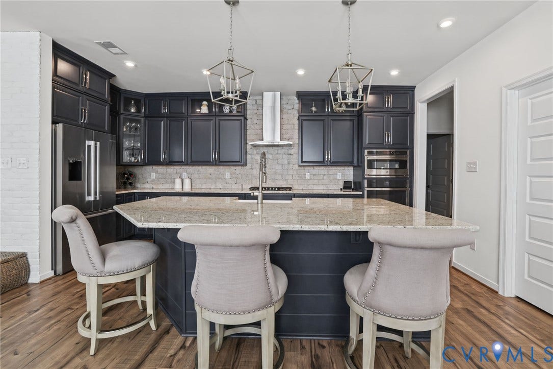 9337 Citrine Run, Henrico, VA 23238 Kitchen featuring dark cabinetry, stone-surface central island, light-toned brick backsplash, stainless steel appliances, and geometric pendant lighting