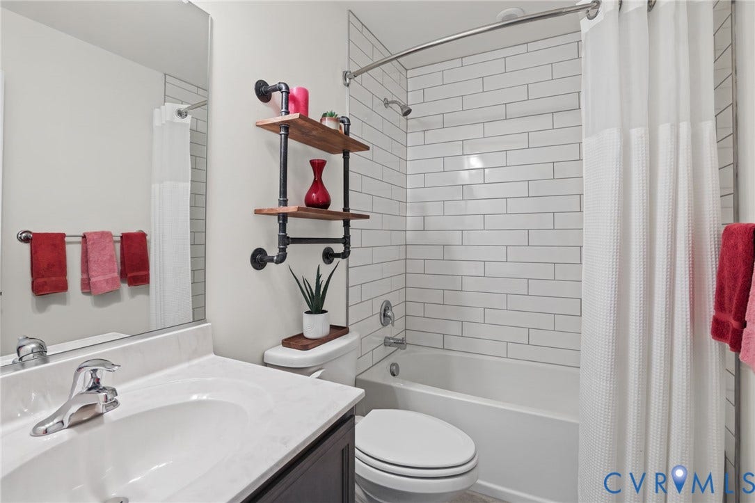 9337 Citrine Run, Henrico, VA 23238 Bathroom featuring a white subway tile shower surround, vanity with a light-toned countertop, integrated basin, large wall-mounted mirror, and industrial-style metal and wood shelving