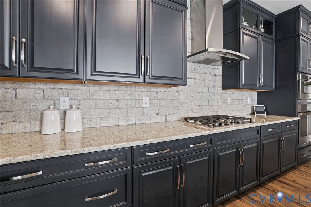 9337 Citrine Run, Henrico, VA 23238 Dark-toned shaker cabinetry with metal hardware, textured brick backsplash, stone countertops, stainless steel gas cooktop, and built-in stainless steel wall oven