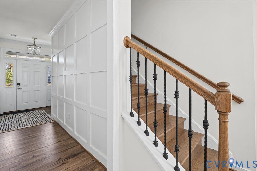 9337 Citrine Run, Henrico, VA 23238 Foyer featuring crisp white wainscoting, wood-finish flooring, staircase with wood handrails and black metal balusters, and a tiered crystal chandelier