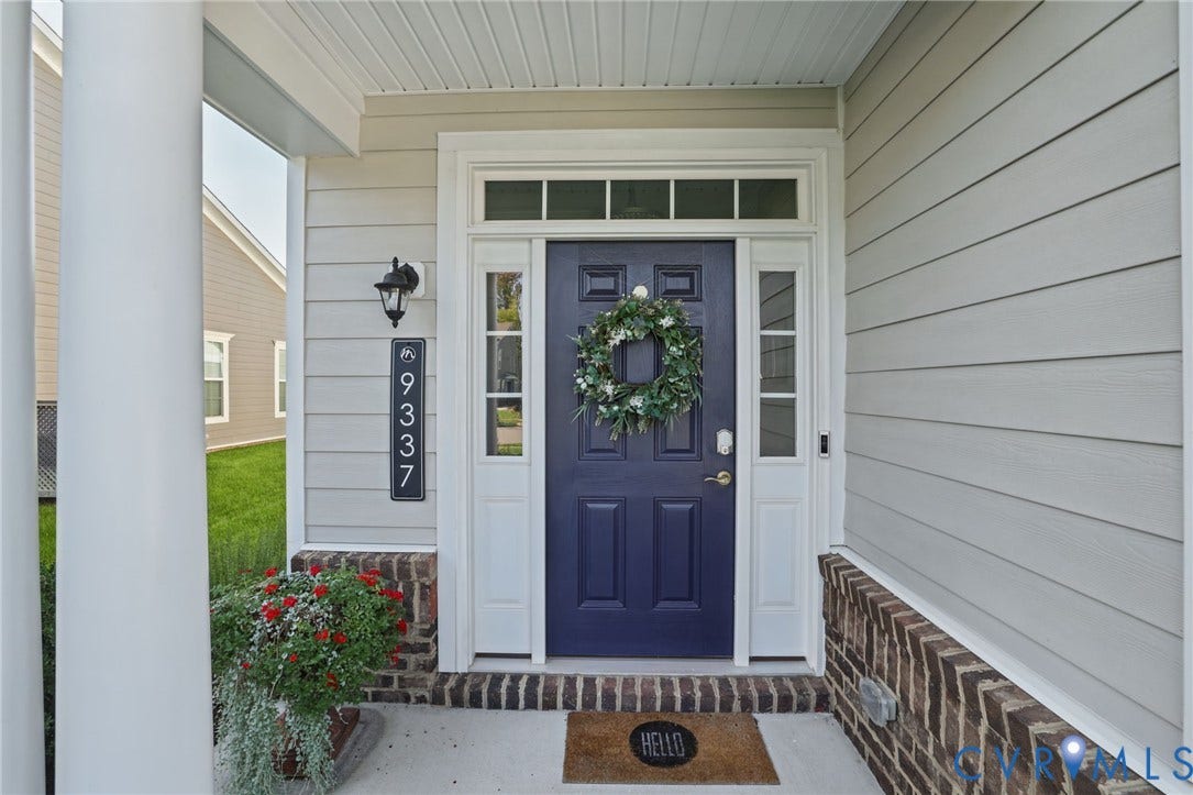 9337 Citrine Run, Henrico, VA 23238 Covered porch entrance featuring lap siding, brick masonry base, dark blue front door with transom and sidelights, and exterior wall-mounted light fixture