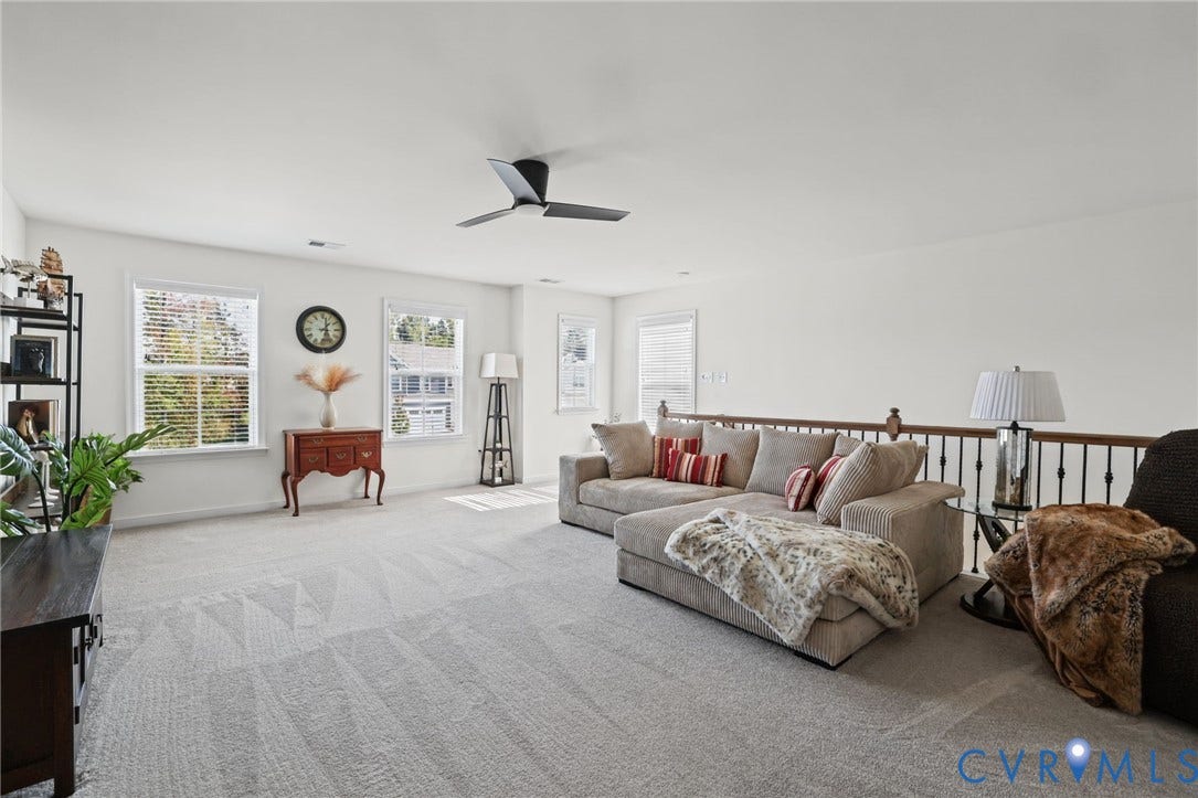 9337 Citrine Run, Henrico, VA 23238 Open-concept area featuring neutral carpeting, a matte black ceiling fan, multiple windows with natural light, and a wooden handrail with metal balusters