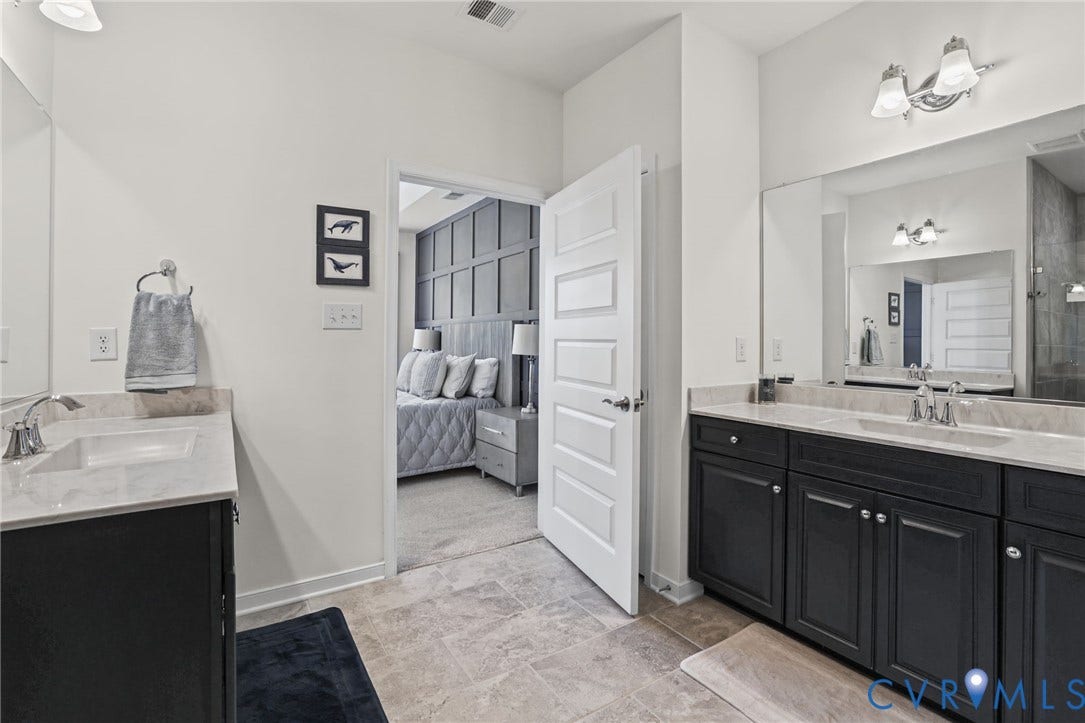 9337 Citrine Run, Henrico, VA 23238 Dual vanity area featuring charcoal cabinetry, light-toned stone-finish countertops, rectangular undermount sinks, and polished chrome fixtures with wide mirrors and wall-mounted lighting
