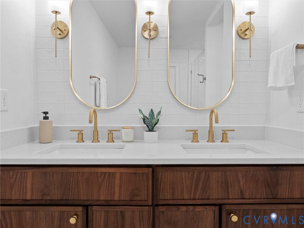 702 Westham Parkway, Westham, Henrico, VA 23229 Dual basin vanity with wood-finish cabinetry, white countertop, gold-finish fixtures, and integrated mirrors with sconce lighting