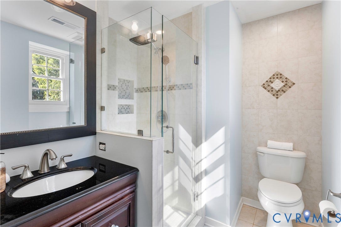 12380 Bienvenue Road, Bowles Acres, Rockville, VA 23146 Bathroom featuring a dark wood-finish vanity, integrated oval sink with metal faucet, frameless glass enclosed shower with recessed shelving, and tiled wall accents