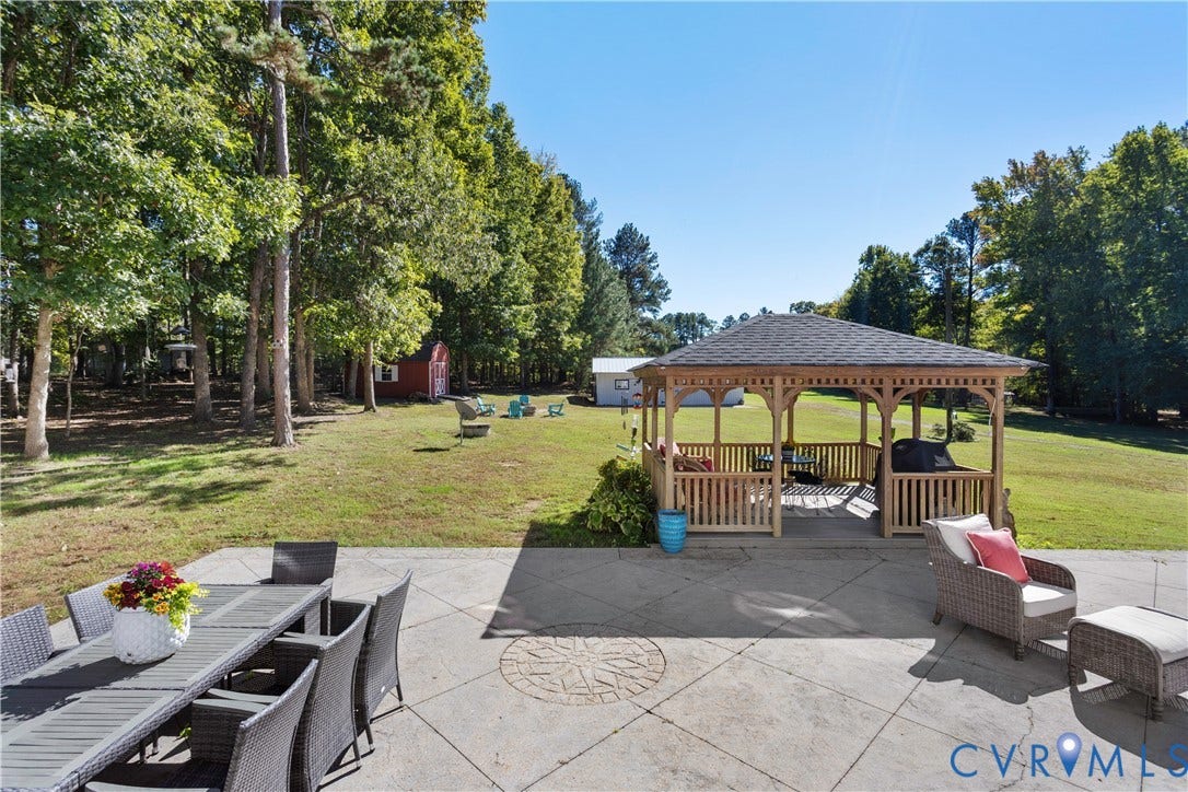 12380 Bienvenue Road, Bowles Acres, Rockville, VA 23146 Expansive backyard featuring a concrete patio with an inlaid stone medallion, a wooden gazebo, mature trees, and detached storage structures