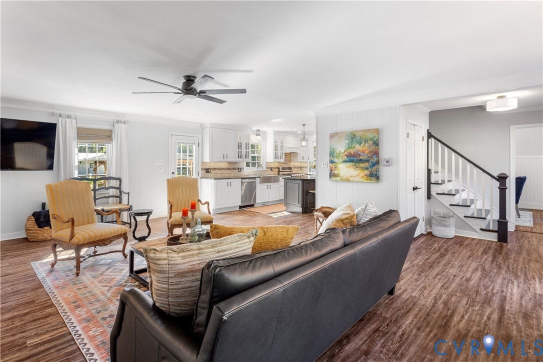12380 Bienvenue Road, Bowles Acres, Rockville, VA 23146 Open-concept main living area featuring LTV flooring, a ceiling fan, white cabinetry with stainless steel appliances, a farmhouse-style kitchen sink, and a staircase with a dark wood handrail and white balusters