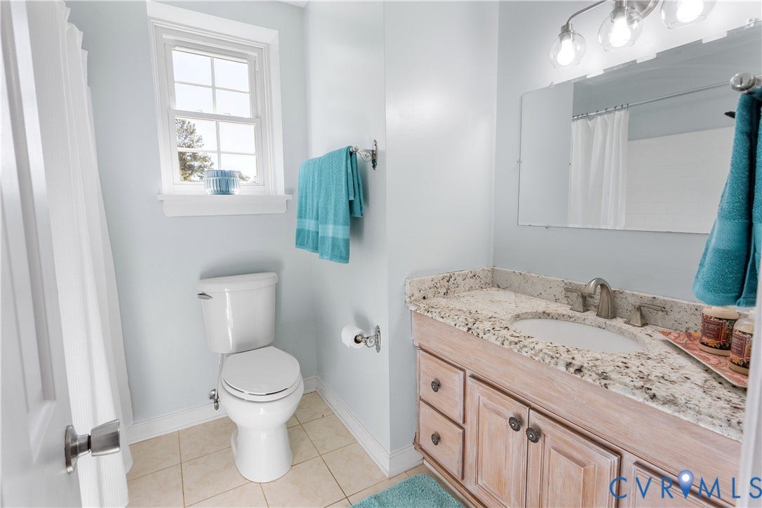 12380 Bienvenue Road, Bowles Acres, Rockville, VA 23146 Bathroom featuring a vanity with stone-finish countertop, light wood-finish cabinetry, tile flooring, and a wall-mounted multi-bulb light fixture