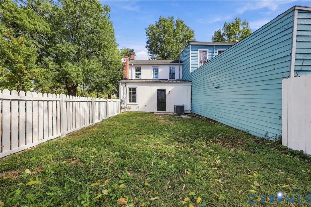 Rear exterior featuring a grass lawn, white picket fencing, and a multi-level siding facade