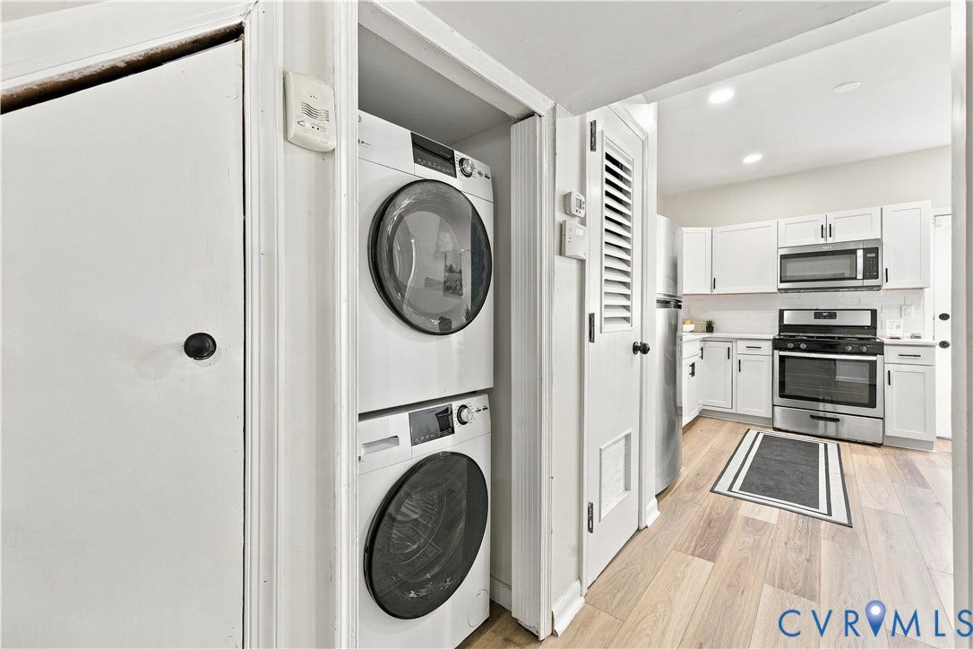 Laundry closet featuring a stacked washer and dryer, wood-finish flooring, recessed lighting, white cabinetry, and stainless steel appliances