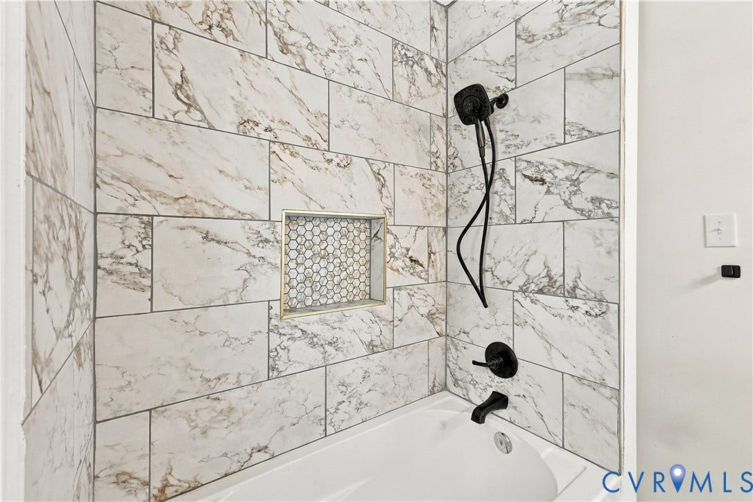 Shower enclosure featuring large-format stone-patterned wall tile, a recessed niche with hexagonal mosaic tile inlay, and matte black plumbing fixtures