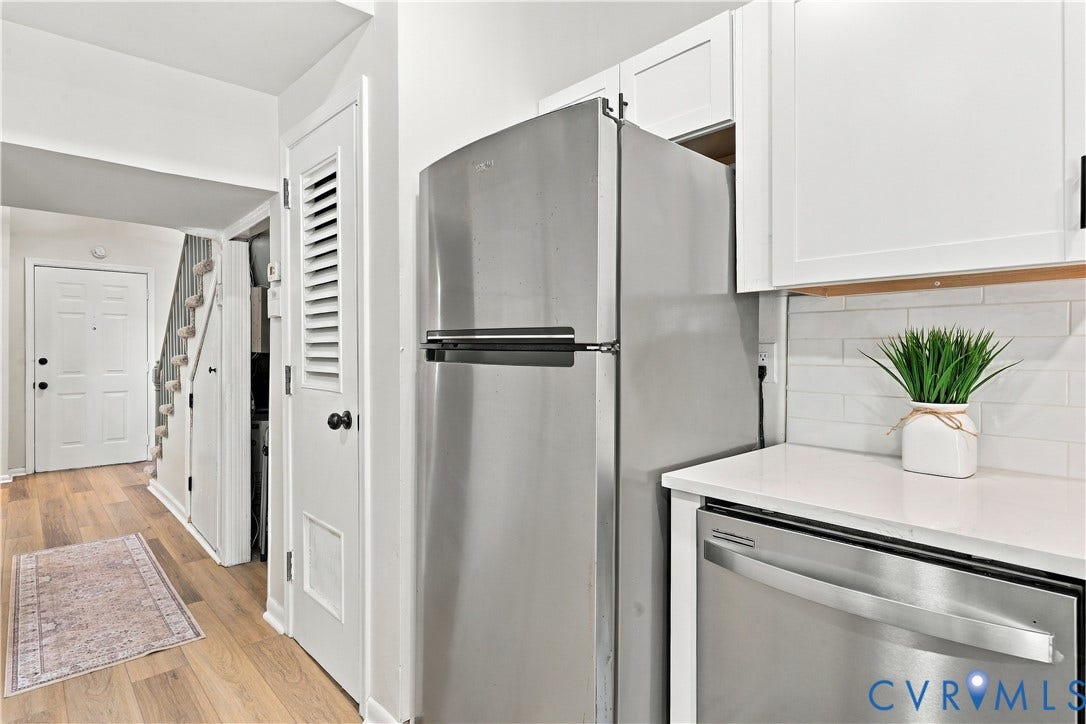 Kitchen featuring stainless steel appliances, white cabinetry, a light-toned solid surface countertop, and a white subway tile backsplash, complemented by wood-finish flooring
