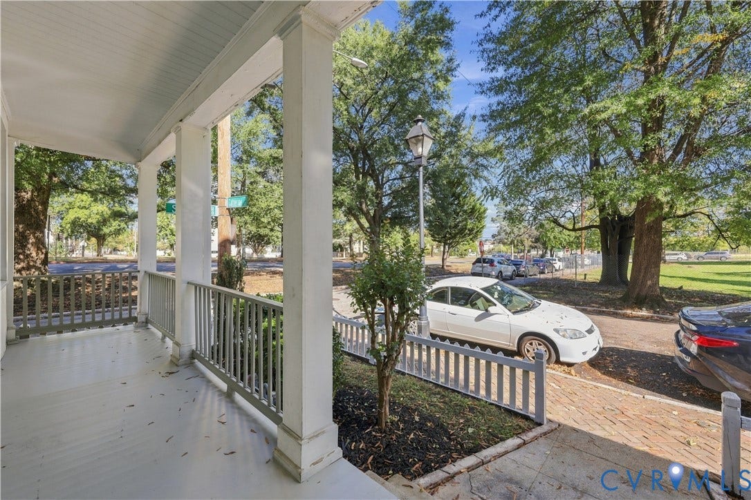 Covered front porch featuring white structural columns, picket-style railing, beadboard ceiling, and brick paver walkway