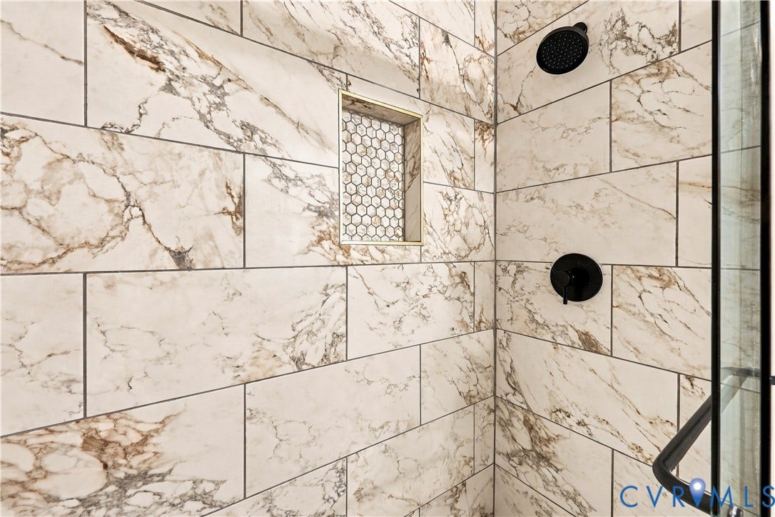 Shower featuring large-format stone-patterned wall tile, inset decorative hexagonal tile niche, matte black rain-style shower head, and matte black temperature control valve