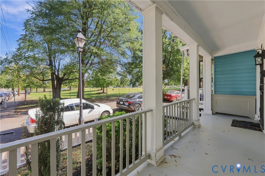 Covered front porch featuring structural columns, wood-finish railing, horizontal siding, and an attached exterior light fixture