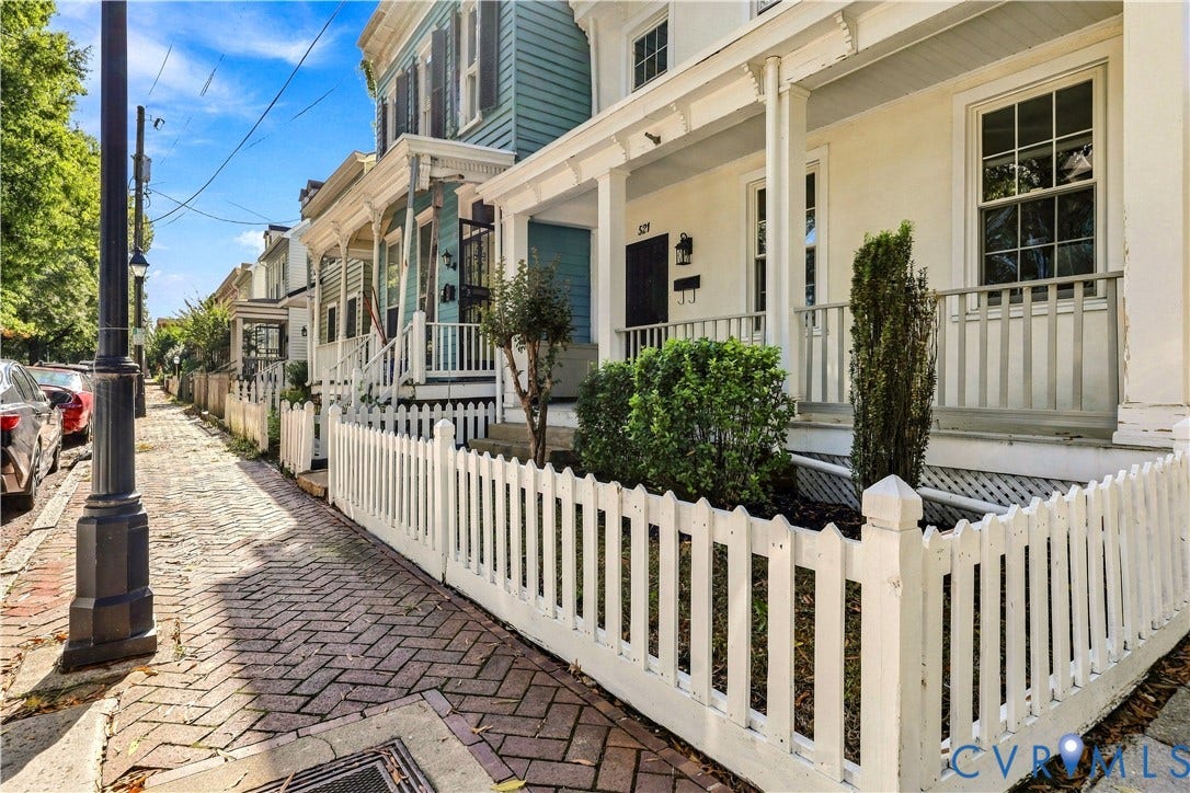 Historic-style home featuring a covered front porch, white picket fencing, and a herringbone-patterned brick walkway