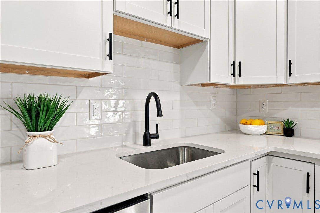 Kitchen featuring white shaker cabinetry with matte black hardware, stone-finish countertops, subway tile backsplash, and an undermount stainless steel sink with a high-arch matte black faucet