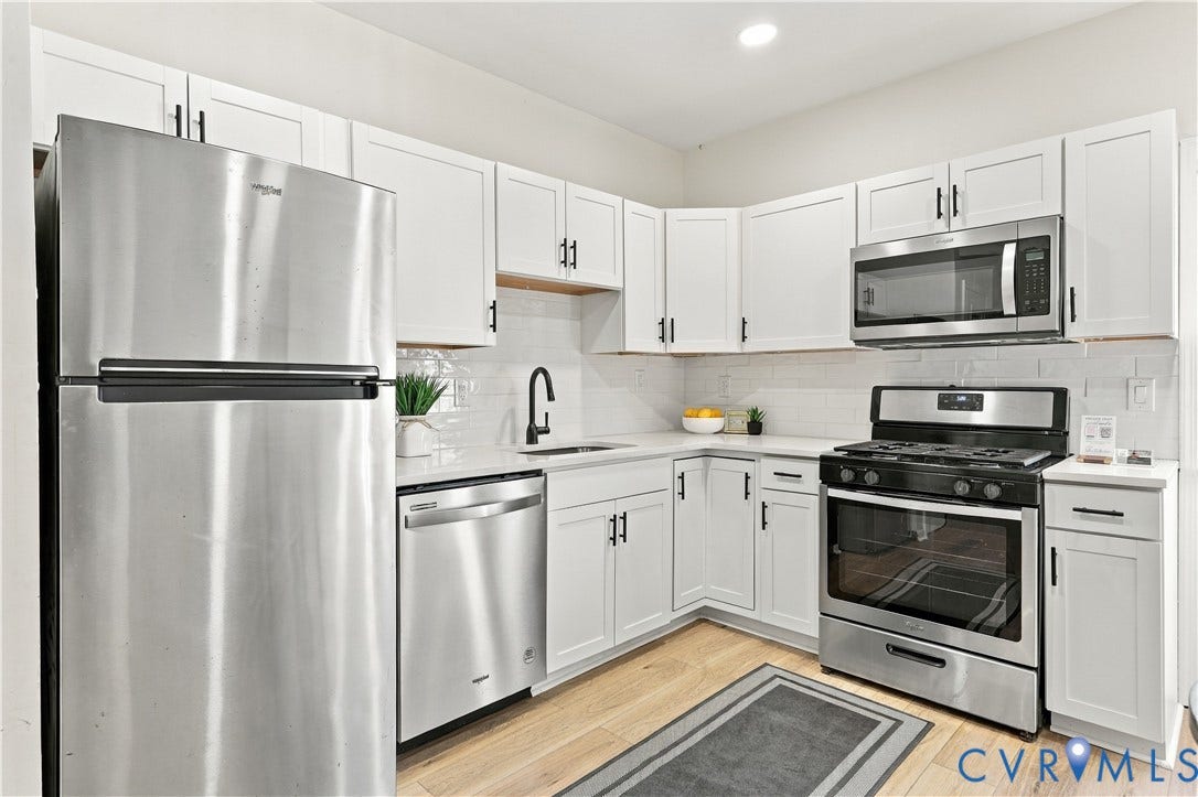 Kitchen featuring white shaker-style cabinetry, solid-surface countertops, subway tile backsplash, stainless steel appliances, and wood-finish flooring