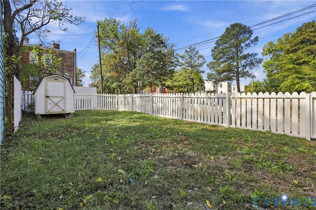 Fenced backyard featuring a white picket fence, a detached storage shed, and mature trees