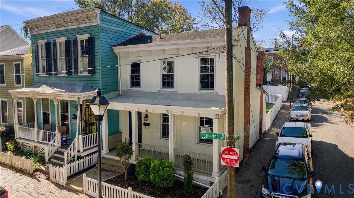 Two-story residence featuring a painted masonry exterior, a covered front porch with decorative millwork, an exposed brick chimney, and white picket fencing